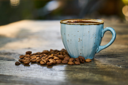 aza de café recién servido sobre mesa con granos de café esparcidos, luz natural y ambiente cálido.